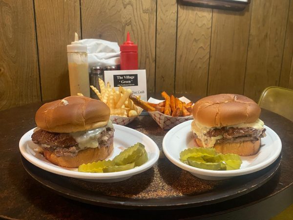 Two burgers on a plate with fries and pickles.