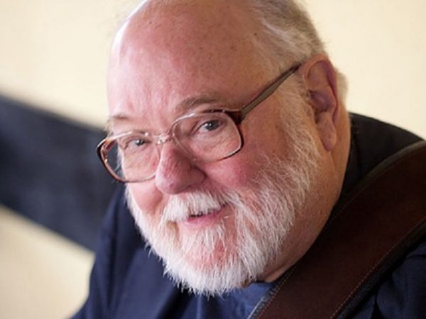 a man with a white beard wearing glasses and a blue shirt.