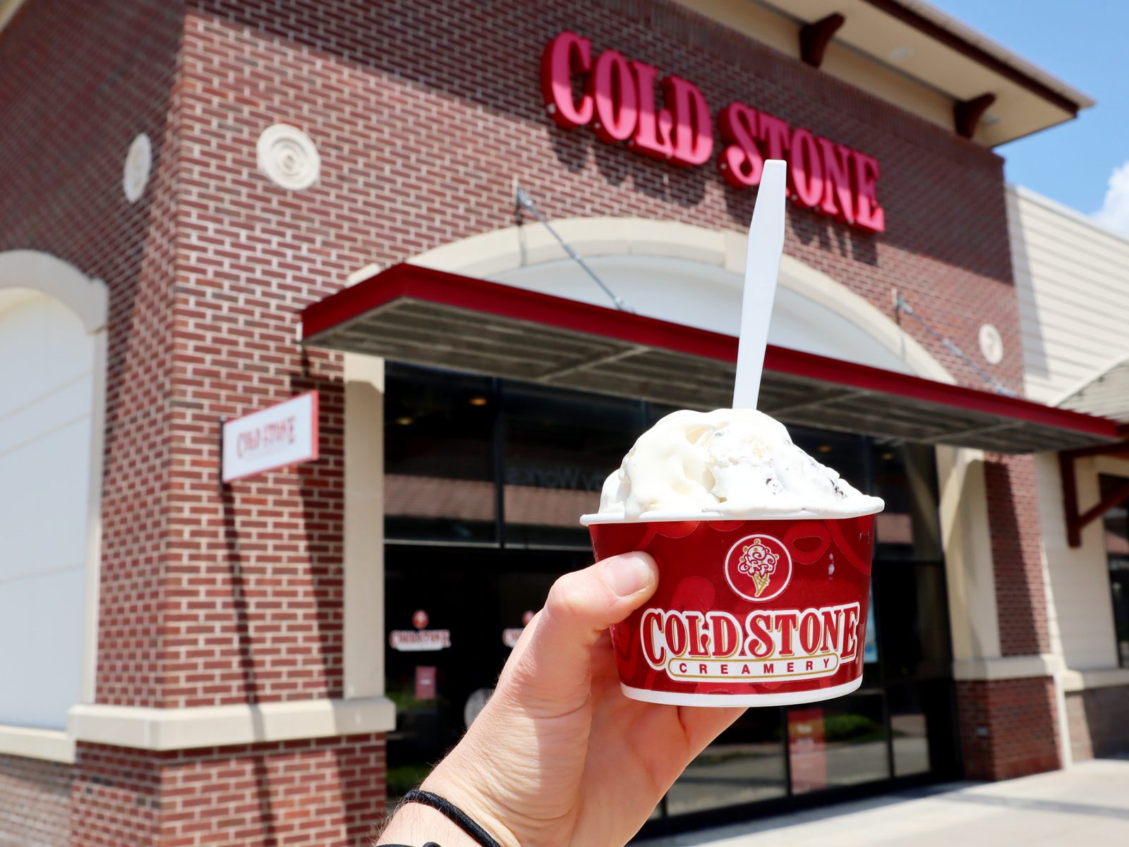 a hand holding a cup of ice cream outside of a store.