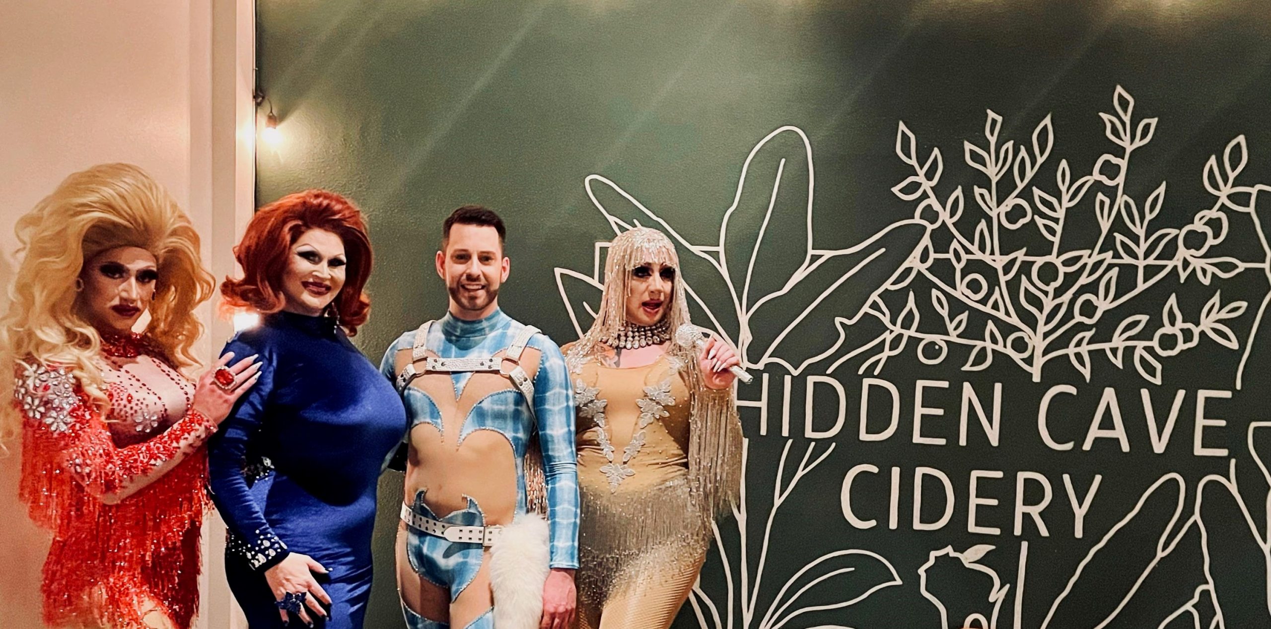 A group of people standing in front of a sign that says hidden cave cidery.