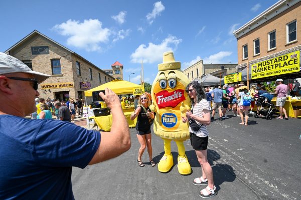 A group of people at the Middleton Mustard Museum taking a picture of a Yellow Mustard mascot, Frenchie.