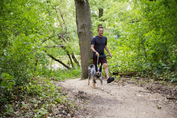 A man walking a dog on a trail in the woods.