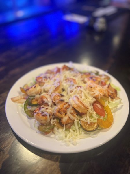 A plate with shrimp, vegetables and cheese on it.
