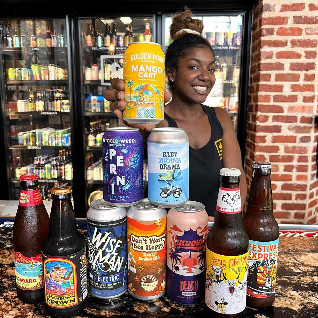 A woman holding a stack of beer cans in front of a bar.